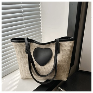 Détail du sac seau en paille tressée avec écusson cœur en cuir noir et fines bandoulières