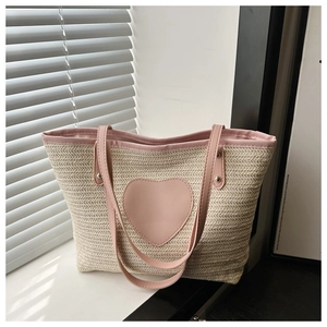 Détail d'un cœur rose sur un sac en paille tissée avec anses en cuir assorties