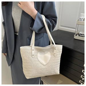 Détail du sac fourre-tout tissé crème avec un écusson cœur, porté par un mannequin en costume