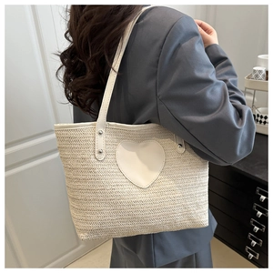 Vue détaillée du sac seau en paille tressée avec patch cœur, porté par une femme en blazer