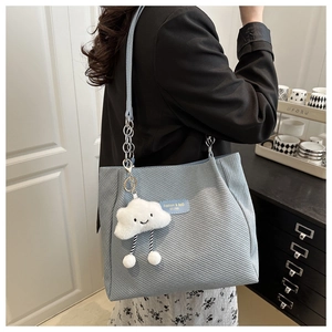 Detail of light blue tote bag featuring twill texture, chain strap, and plush cloud charm