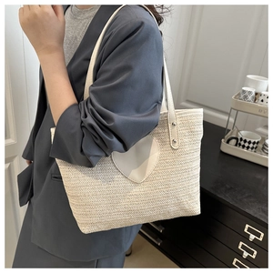 Vue détaillée d'un sac cabas en paille beige avec patch cœur blanc porté à l'épaule
