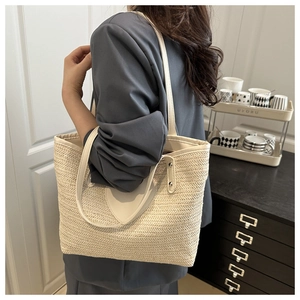 Détail d'un sac cabas en paille avec bordure en cuir crème porté à l'épaule par un mannequin
