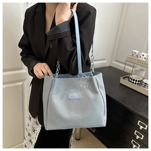 Detail of light blue tote bag with textured fabric, leather label, and silver metal chain