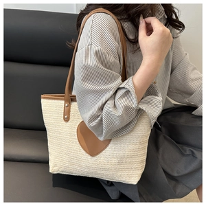 Détail du sac seau tressé en paille crème avec cœur en cuir marron et poignées