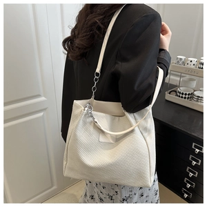 Detail of a beige corduroy tote bag with slim leather straps and metal chain