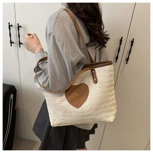 Détail d'un sac cabas en paille tissée avec un grand empiècement cœur en cuir marron