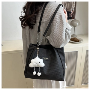 Detail of black textured tote bag with metal chain strap and white plush cloud charm