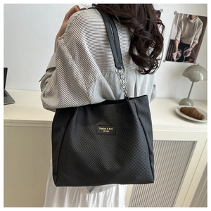 Detail of a black twill fabric tote bag with elegant gold logo and chain strap