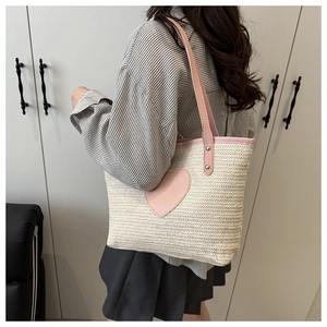 Gros plan du sac cabas en paille avec écusson cœur rose et poignées en cuir robustes pour femme
