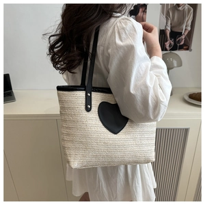 Détail d'un sac cabas en paille avec un patch coeur noir et une poignée de transport