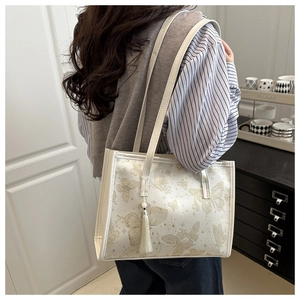 Detail of off-white tote bag featuring golden butterfly prints and decorative white tassel