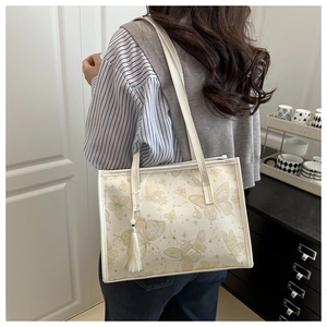 Detail of white tote bag with gold butterfly print and tassel on model shoulder