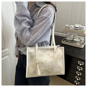Borsa tote bianca con motivo farfalla dorata e frange, indossata a spalla elegante