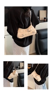 Detail of beige crescent underarm bag with decorative metal buckles and rivets