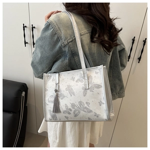 Dettaglio della borsa tote argento con stampe a farfalla e nappa decorativa sulla tracolla