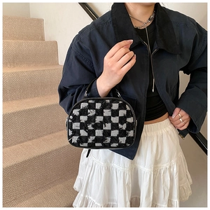 Detail of checkered tweed texture and metal zipper on a compact crossbody bag