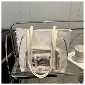 Detail of cream shoulder bag featuring a clear PVC window with a plush cat paw charm inside