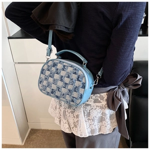 Detail view of small blue plaid crossbody bag worn by model in a modern home setting