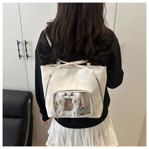 Detailed back view of a white ita bag featuring a clear PVC window with a plush cat accessory
