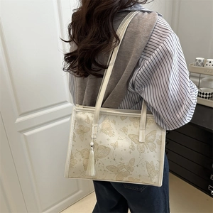 Borsa tote bianco sporco con ricamo a farfalla dorata e nappe indossata da una modella