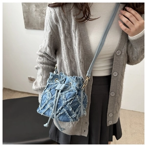 Close-up of denim bucket bag with frayed tassel diamond pattern and leather strap