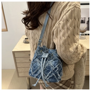 Detailed close-up of blue denim bucket bag with quilted distressed patchwork and tassels
