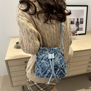 Blue denim quilted bucket bag with tassel drawstring on female model in a home setting