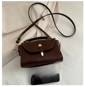 Close-up of vintage brown crossbody bag next to a smartphone for size comparison