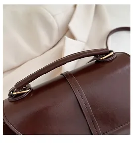 Detailed close-up of dark brown handbag showing oily leather texture and golden buckle