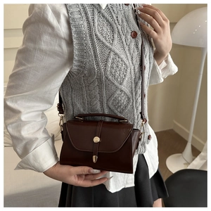 Close-up of a vintage dark coffee crossbody bag with gold hardware worn by a model