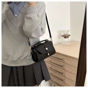 Detail of minimalist black crossbody bag with golden clasp and wide top handle grip
