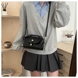 Detail of black leather crossbody bag with gold teardrop buckle in a cozy home setting