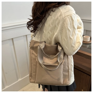 Detail of a large beige nylon tote bag with front flap pocket shown on a model