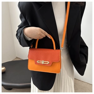 Model wearing orange textured crossbody bag with gold buckle and modern black blazer outfit