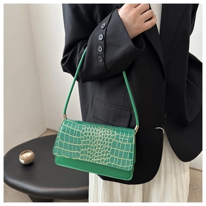 Detail of a green croc-effect shoulder bag worn with a black blazer and white skirt