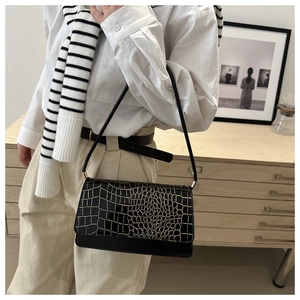 Detail of a vintage black crocodile pattern shoulder bag worn with a casual chic outfit