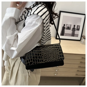 Close-up of black croc-embossed underarm bag with gold grid detail on white shirt