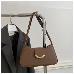 Detailed shot of brown matte leather shoulder bag with gold crescent buckle on clothing rack