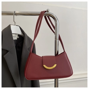 Detail of burgundy underarm bag with gold crescent buckle on a dark grey blazer background