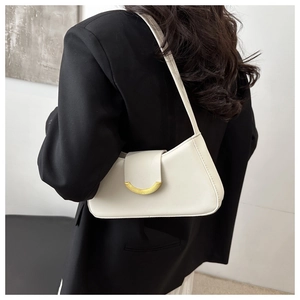 Detail of a creamy beige underarm bag with a gold metal clasp on a model in a black blazer