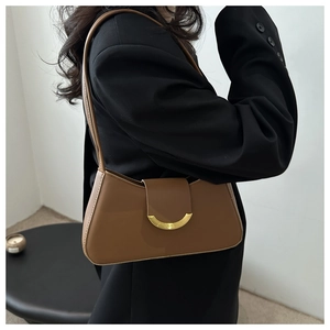 Detail of a brown leather shoulder bag with a gold crescent buckle on a black blazer
