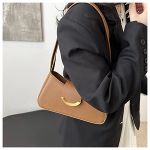 Detail of tan leather underarm bag featuring a gold half-moon buckle worn over the shoulder