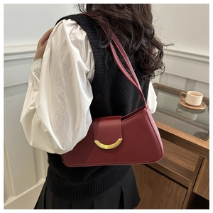 Detail view of burgundy leather underarm bag with gold crescent buckle on a shoulder model
