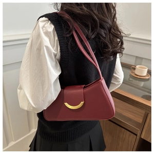Model wearing a burgundy matte leather baguette underarm bag with gold crescent buckle