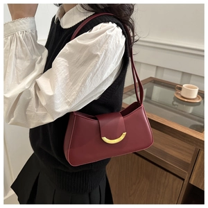 Detail of burgundy underarm bag with gold buckle on a model in a cozy indoor setting