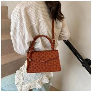 Dettagli del motivo in pelle marrone goffrata e del manico intrecciato della borsa a tracolla