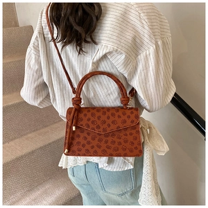 Detail of vintage embossed pattern on dark brown square shoulder bag worn by model