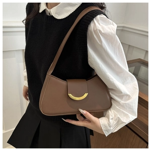 Detail of a brown leather underarm bag with a gold half-moon buckle worn by a model