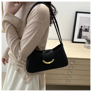 Detail of a minimalist black leather underarm bag with an elegant golden crescent buckle